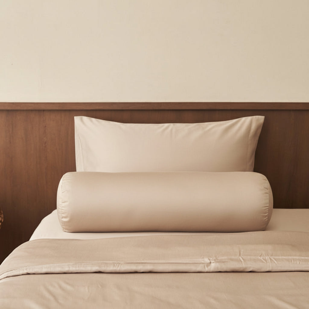 Two beige TENCEL NAIA pillows stacked on a bed with a wooden headboard.