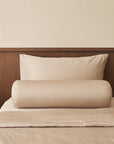 Two beige TENCEL NAIA pillows stacked on a bed with a wooden headboard.