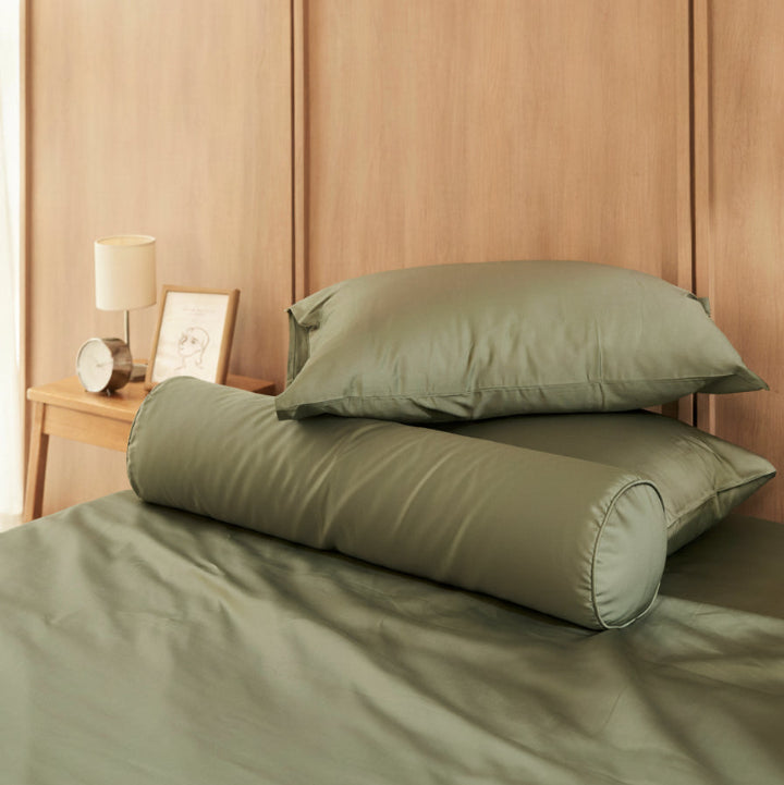 Two green pillows on a bed in a bedroom setting with wooden walls and a side table.