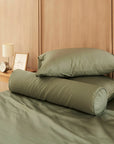 Two green pillows on a bed in a bedroom setting with wooden walls and a side table.
